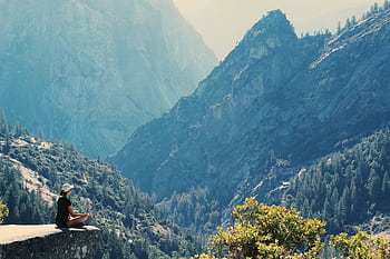 A woman practices meditation on a cliff edge, surrounded by majestic mountains and serene nature. HD wallpaper