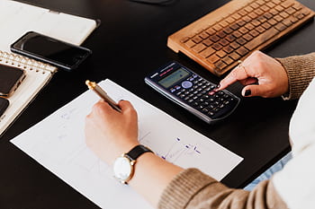 Close-up of hands working with a calculator and notebook on a desk, analyzing documents. HD wallpaper