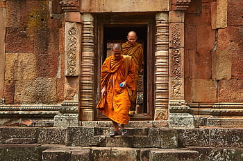 Buddhist monks in orange robes step out of an ancient stone temple in Thailand, showcasing historical architecture. HD wallpaper