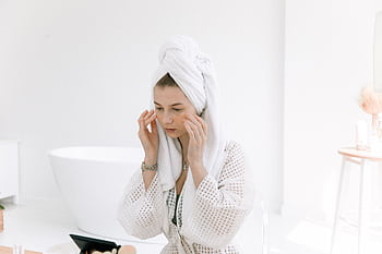 Woman in white bathrobe applying skincare in a bright bathroom. Perfect for wellness and beauty themes. HD wallpaper