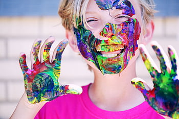 A joyful child with vibrant face paint and hands, expressing happiness and creativity. HD wallpaper