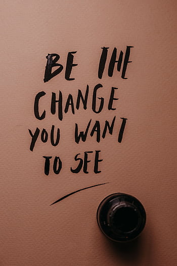 Inspirational message 'Be the change you want to see' in black ink on pink surface. HD phone wallpaper