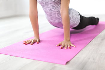 A woman performs a yoga stretch indoors on a pink mat, promoting a healthy lifestyle. HD wallpaper