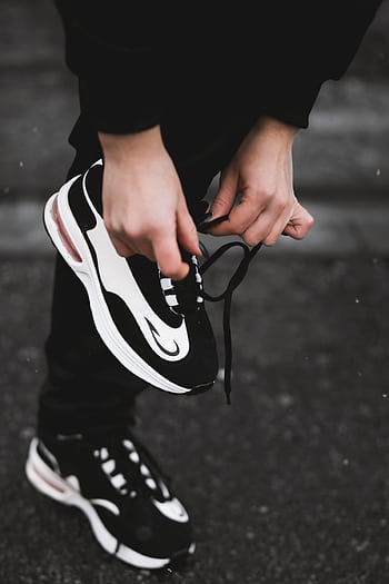 Close-up of an athlete tying black and white sneakers on a street, highlighting fitness and outdoor exercise. HD phone wallpaper