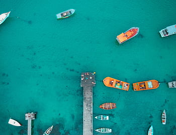 Aerial shot of vibrant boats docked in turquoise waters at a wooden pier in Vila Nova, Brazil. HD wallpaper