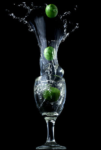 Lime splashing into water in a cocktail glass, creating dynamic motion against a black background. HD phone wallpaper