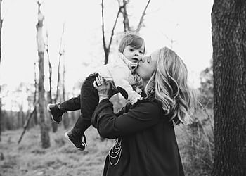 A touching moment of a mother kissing her young child in a serene outdoor setting captured in black and white. HD wallpaper
