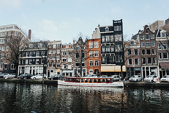 Charming Amsterdam canal scene with classic Dutch architecture and a boat cruising on the water. HD wallpaper