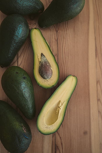 Sliced avocados showcasing fresh, vibrant green flesh on a wooden surface. HD phone wallpaper