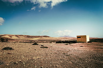 A solitary concrete bunker stands isolated in a barren desert landscape under a clear sky. HD wallpaper
