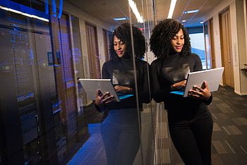 African American woman standing in modern office using laptop, reflecting professionalism and technology engagement. HD wallpaper