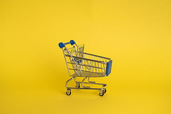 A small metallic shopping cart on a vivid yellow background, representing retail and commerce. HD wallpaper