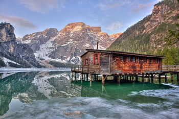 A serene lakeside cabin reflecting on water surrounded by majestic mountains. HD wallpaper