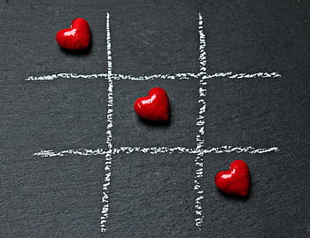 Tic tac toe board on black surface with red heart shapes symbolizing love and connection. HD wallpaper