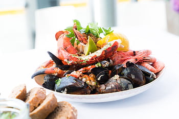 A vibrant seafood platter featuring lobster, shrimp, mussels, and lemon on a white plate. HD wallpaper