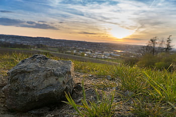 Close-up of a rock on grassy terrain with a scenic sunset in the background. HD wallpaper
