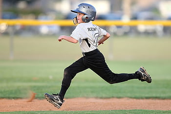 Action shot of a young baseball player running fast on the field, wearing uniform and helmet. HD wallpaper