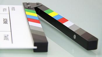 Colorful clapper board on a white surface, used in filmmaking. Ideal for entertainment and movie themes. HD wallpaper