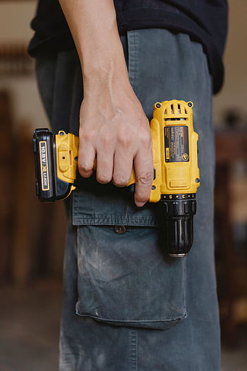 An artisan holding a yellow power drill, showcasing craftsmanship and tool usage. HD phone wallpaper