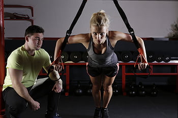 A woman performing strength training with a trainer in a gym setting, showcasing fitness and dedication. HD wallpaper