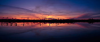 A breathtaking sunset reflecting over a tranquil lake in Alabama, showcasing vibrant colors. HD wallpaper