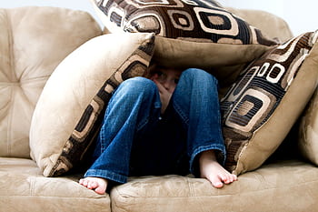 A child crouched under cushions on a couch, conveying a sense of playfulness or fear. HD wallpaper