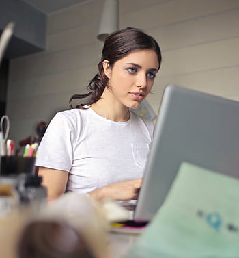Young woman attentively working on her laptop in a cozy indoor setting. HD phone wallpaper