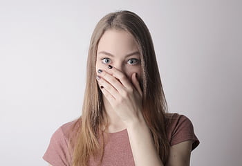 Young woman in pink shirt expressing shock with hand over mouth on simple gray background. HD wallpaper