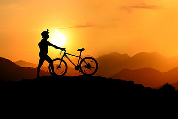Silhouette of a mountain biker at sunset, showcasing adventure and nature's beauty. HD wallpaper