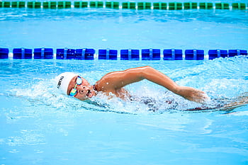A swimmer energetically performs a style stroke in a clear outdoor swimming pool, showcasing competitive spirit. HD wallpaper