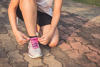 Adult woman tying pink laces on running shoes outdoors. Focuses on fitness and lifestyle. HD wallpaper