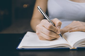 Woman writing in a notebook, capturing a moment of focused concentration. HD wallpaper
