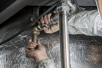 Close-up of a plumber's hands installing steel pipes indoors, showcasing skilled manual work. HD wallpaper