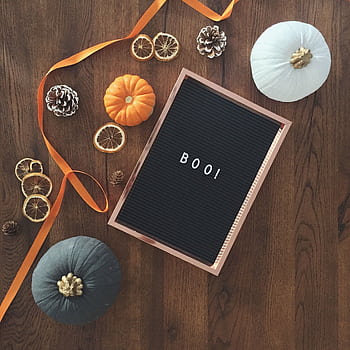 Top-down view of a festive Halloween display featuring pumpkins, pine cones, and the text 'BOO!' on a wooden table. HD phone wallpaper