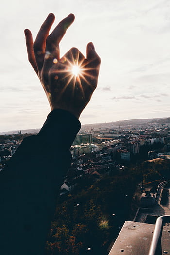 Hand reaching towards sunbeam over cityscape, creating a scenic and dramatic urban view. HD phone wallpaper