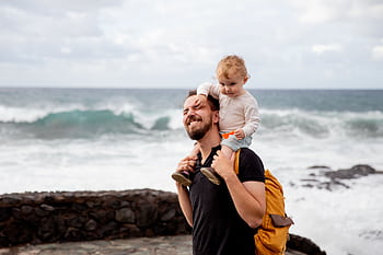 A joyful father and child enjoying time together by the ocean, capturing precious bonding moments. HD wallpaper