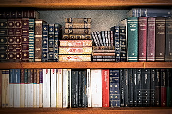 A detailed view of a bookshelf with vintage and classic books arranged neatly, offering a historic ambiance. HD wallpaper