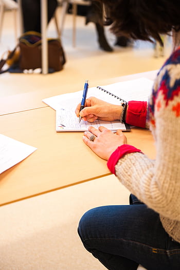 A woman writing notes in a notebook during a classroom lecture setting. HD phone wallpaper