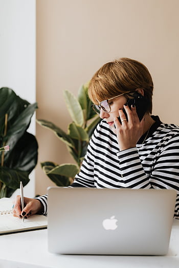 Female entrepreneur on call while taking notes on laptop indoors. HD phone wallpaper