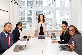 Multicultural team collaborating in boardroom with laptops, showcasing teamwork and diversity. HD wallpaper