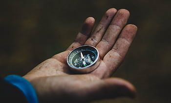 A close-up of a compass held in a dirty hand, symbolizing adventure and navigation. HD wallpaper