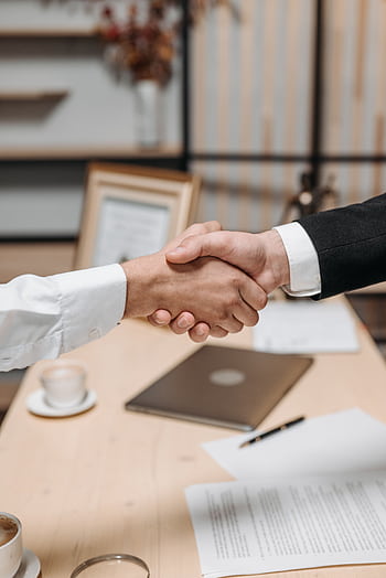 Close-up of two people shaking hands in an office, symbolizing agreement and partnership. HD phone wallpaper