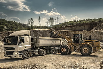 Excavator and truck working together in a quarry, showcasing industrial equipment and operations. HD wallpaper