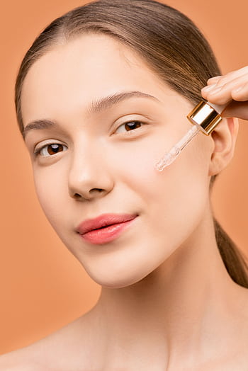 Close-up of a young woman using a dropper to apply facial serum for skincare treatment. HD phone wallpaper