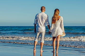 A couple enjoying a romantic walk along the seashore, holding hands and barefoot on the sand. HD wallpaper