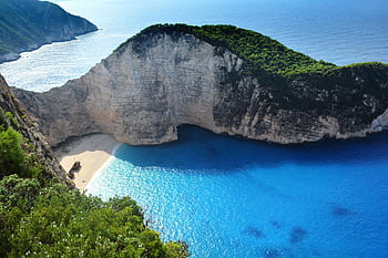 A breathtaking aerial view of Navagio Beach with turquoise waters and lush greenery. HD wallpaper