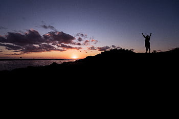 Silhouette of a person celebrating at a stunning sunset by the ocean. HD wallpaper