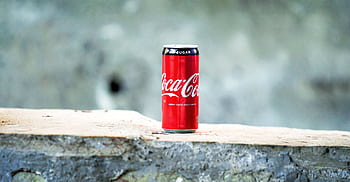 A can of Coca Cola placed on a rough concrete surface with a blurred background. HD wallpaper