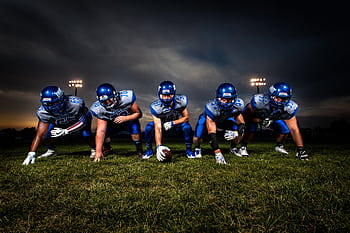 A cohesive football team lines up on the field under stadium lights, prepared for the game ahead. HD wallpaper