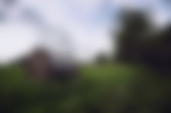 A serene blurred landscape featuring a rustic cabin surrounded by greenery. HD wallpaper